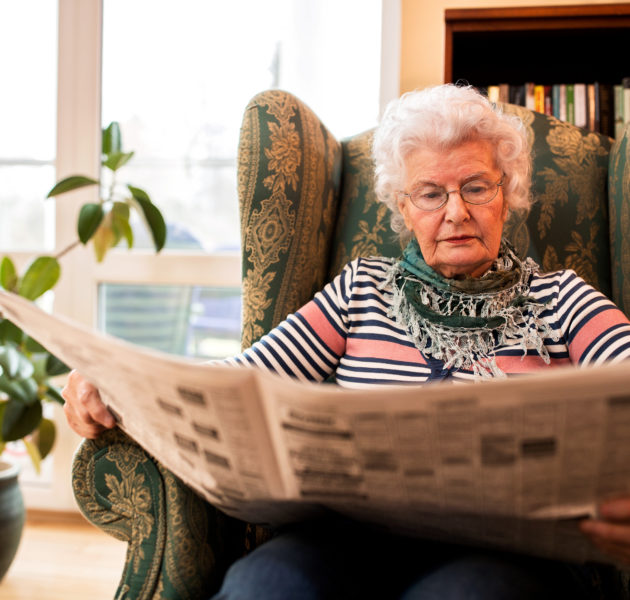 Senior woman in pansion relaxing at home while reading a newspaper