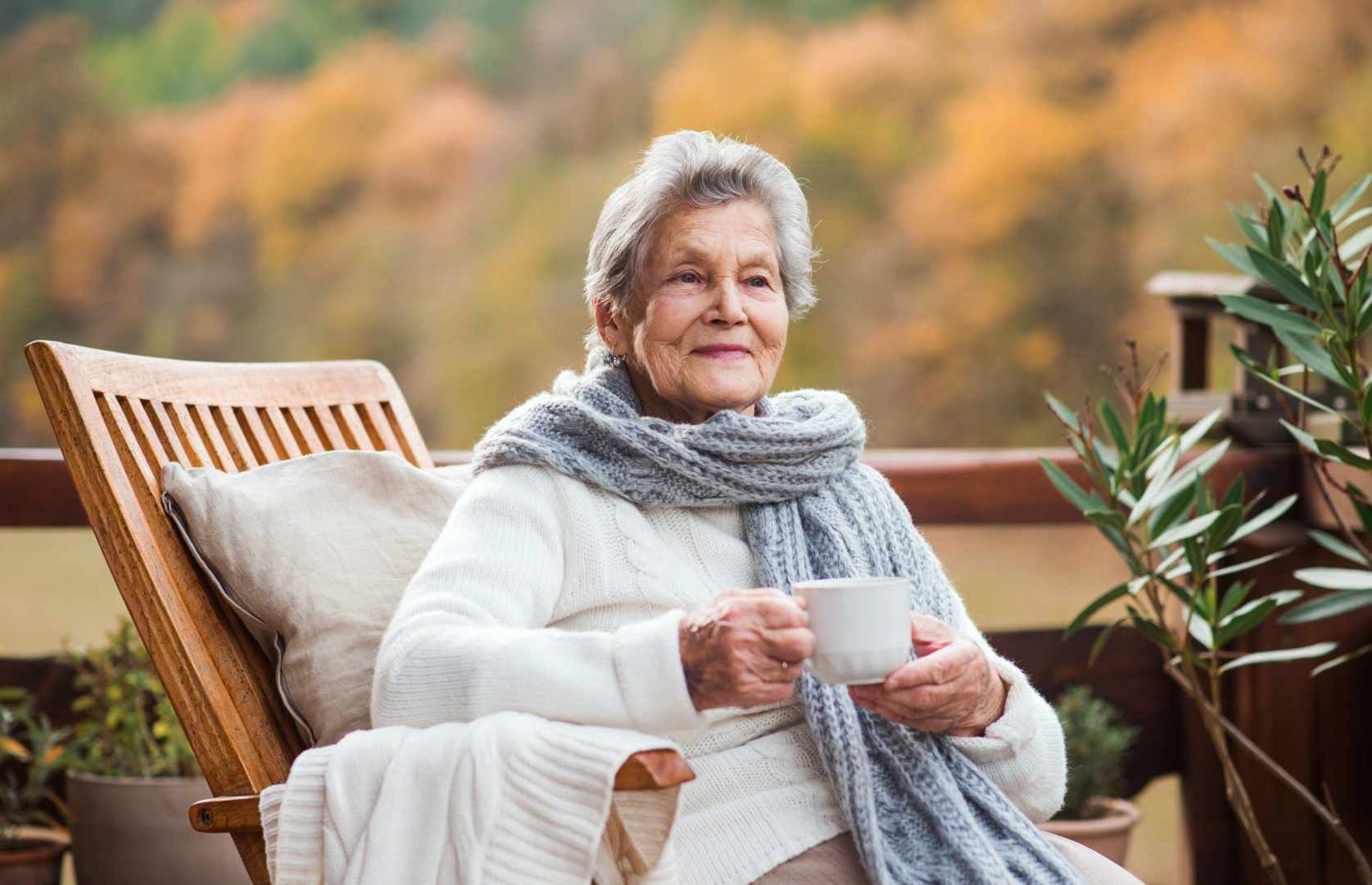 An elderly senior woman sitting outdoors on a terrace in on a sunny day in autumn.